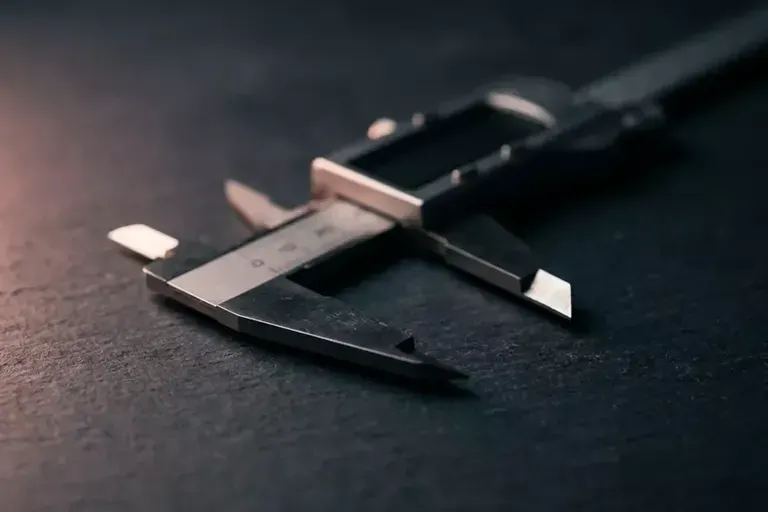 Close-up of a silver caliper on a dark surface, its jaws open at the tip.